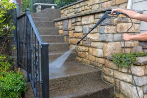 The nozzle of a pressure washer spraying stone steps outside a home.
