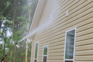 A long pressure washing nozzle spraying water at a home's wooden siding.