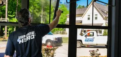 A Window Hero professional inside a home, cleaning a ground floor window with a squeegee.