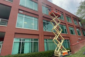A Window Hero professional using a large hydraulic scissor lift to reach the top windows of a three-storey building.