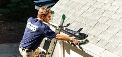 A Window Hero professional at the top of a ladder finishing installation of a gutter guard.