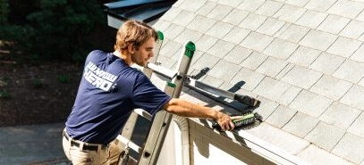 A Window Hero professional at the top of a ladder finishing installation of a gutter guard.