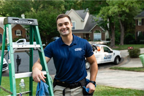 A Window Hero professional smiles as he leans against a small green ladder.
