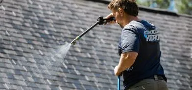A Window Hero professional uses a low-pressure washer to clean a home's roof.