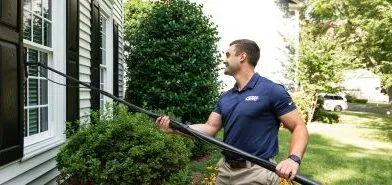 A Window Hero professional uses specialized equipment to clean a ground floor window of a home.