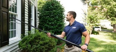 A Window Hero professional uses specialized equipment to clean a ground floor window of a home.