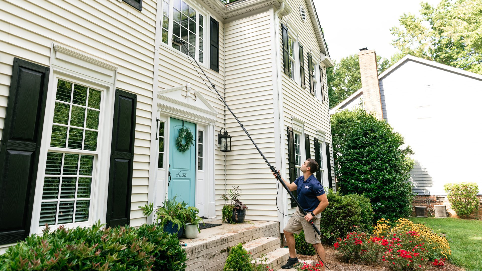 A Window Hero professional uses a telescopic tool to clean the second floor window of a large home.