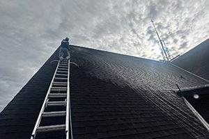 A Window Hero professional climbs up a large sloping roof using a specialized ladder.