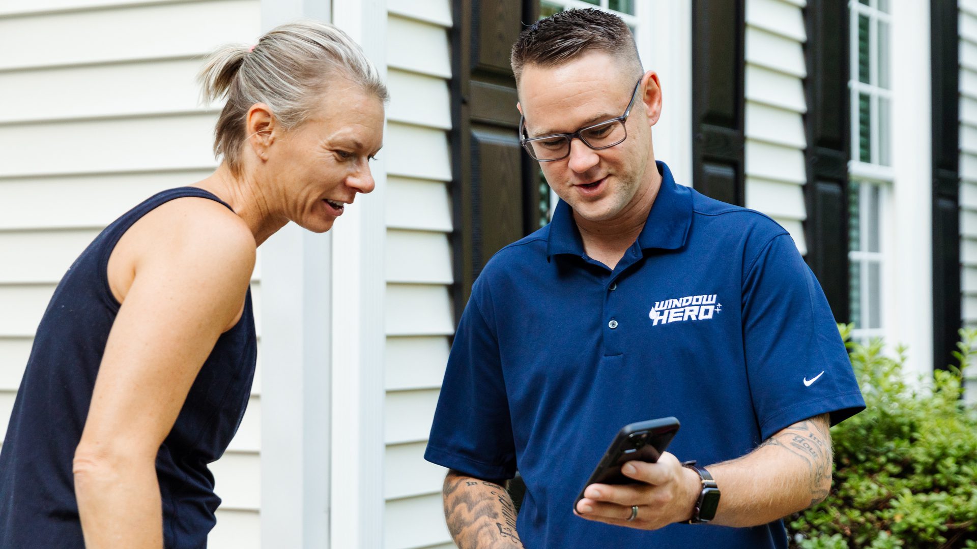 A Window Hero professional showing something to a homeowner on his smartphone.